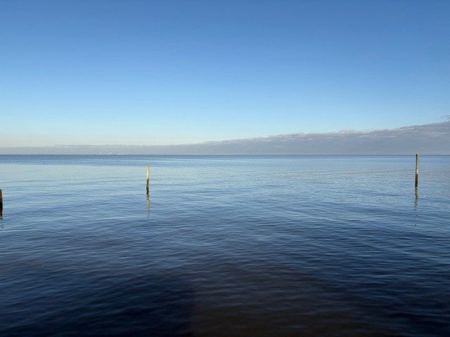 Calm blue water on Mobile Bay with wooden pilings and a clear sky